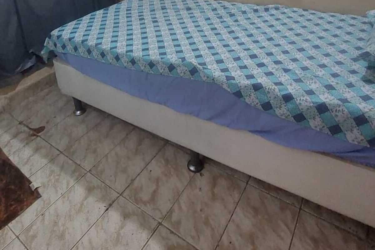 A small, single-bed room with a patterned bedspread, a curtain, and a tiled floor.