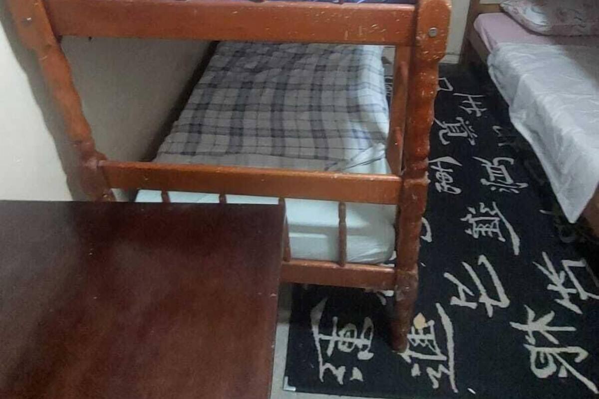 A dormitory room with a wooden bunk bed, a small desk, and a patterned rug.