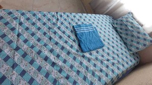 Una habitación pequeña con dos camas individuales, una cama grande con colcha estampada y una ventana con cortinas.