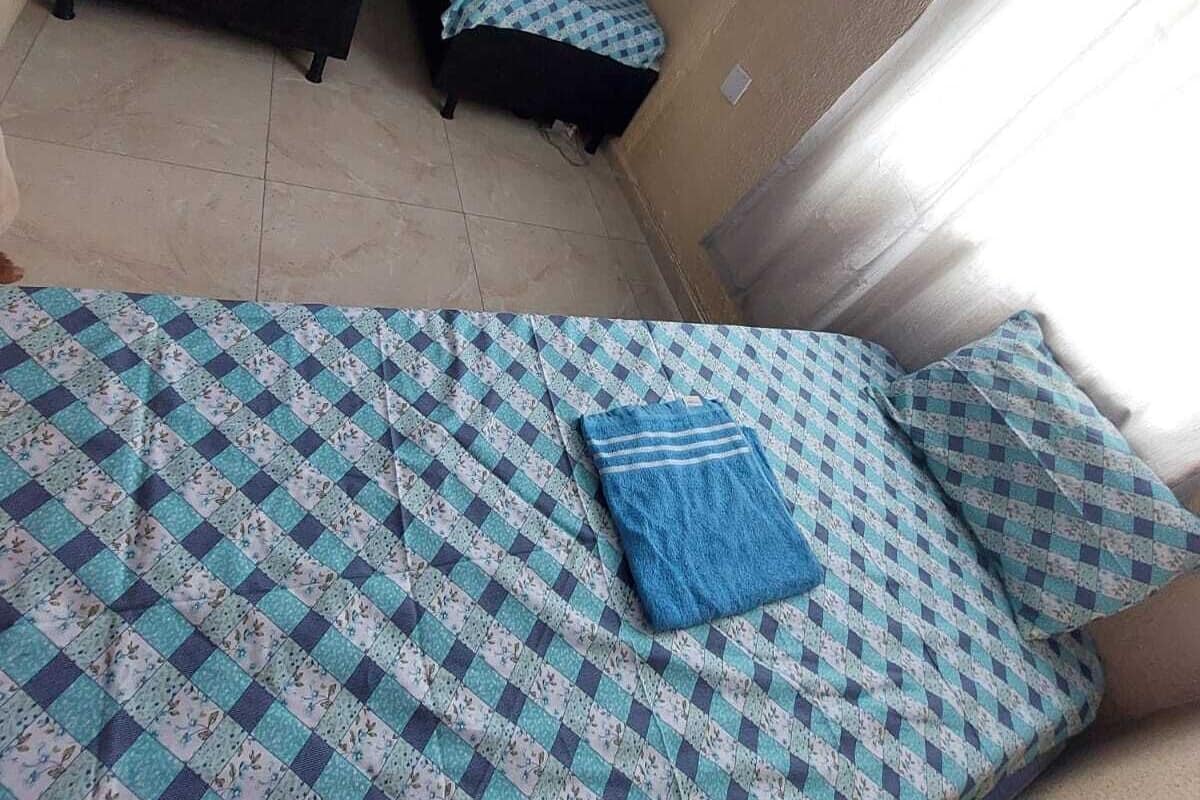 A small room with two single beds, a large bed with a patterned bedspread, and a window with curtains.