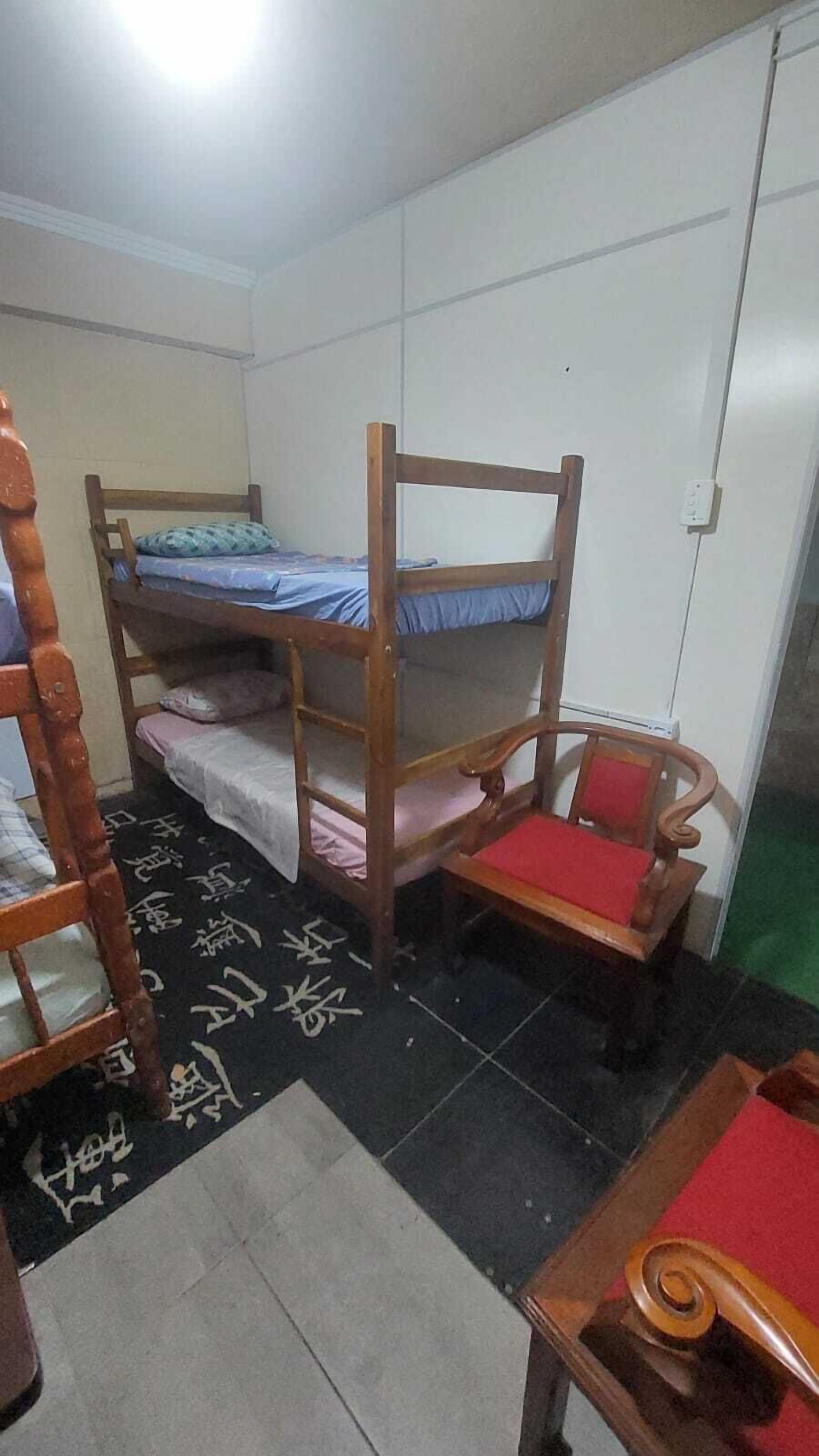 Un dormitorio con literas, una silla de madera, una mesita y suelo de baldosas.