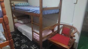 Un dormitorio con literas, una silla de madera, una mesita y suelo de baldosas.
