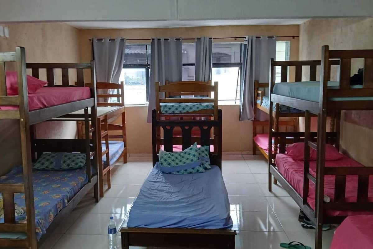 A dormitory room with bunk beds, a central bed, and a window with curtains.