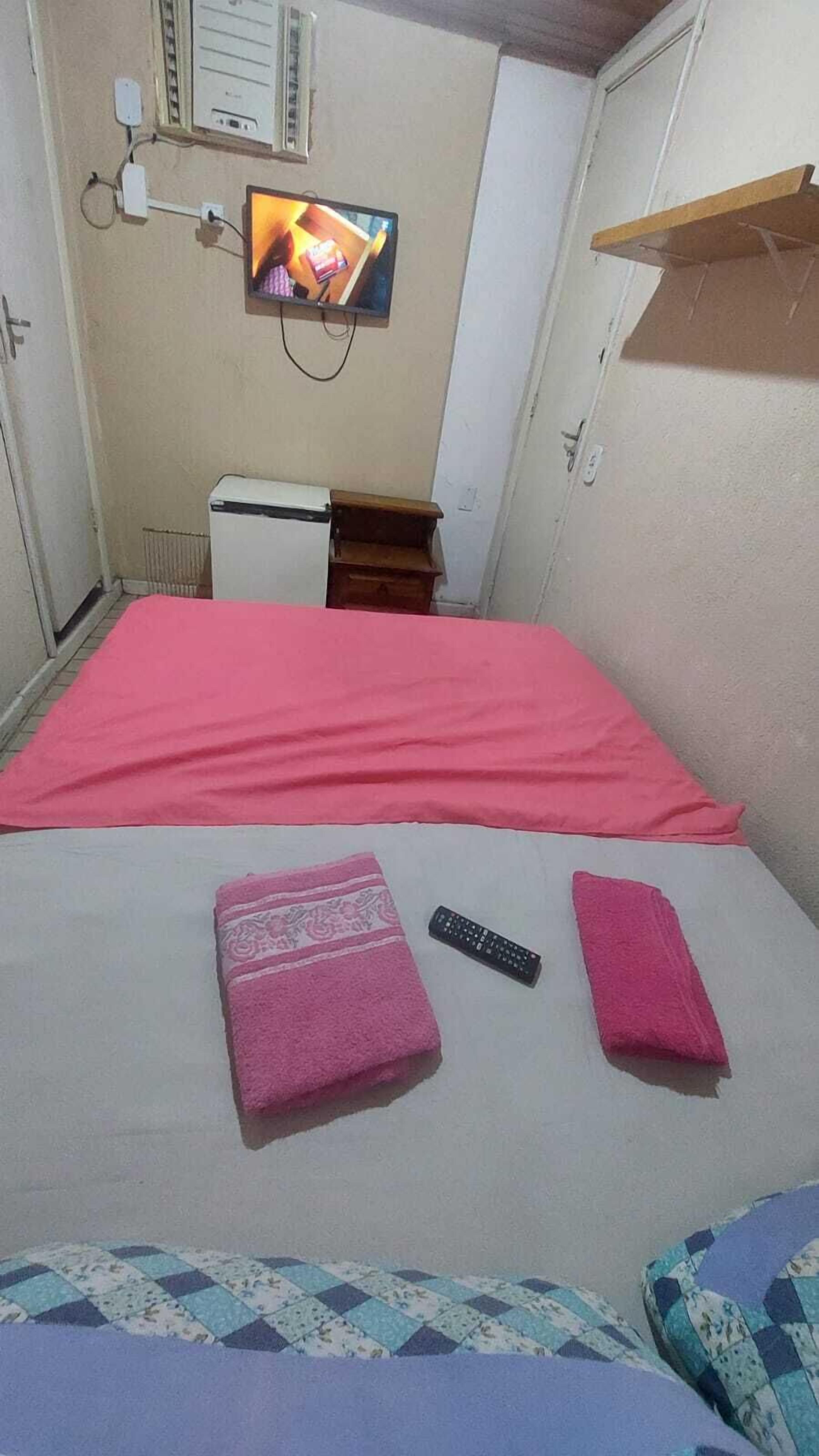 Una habitación pequeña y acogedora con una cama, un televisor montado en la pared y un pequeño calentador.