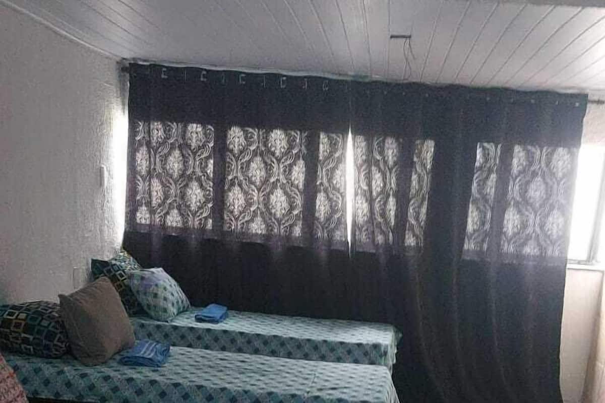 A room with two beds, a small table, and a window with curtains.