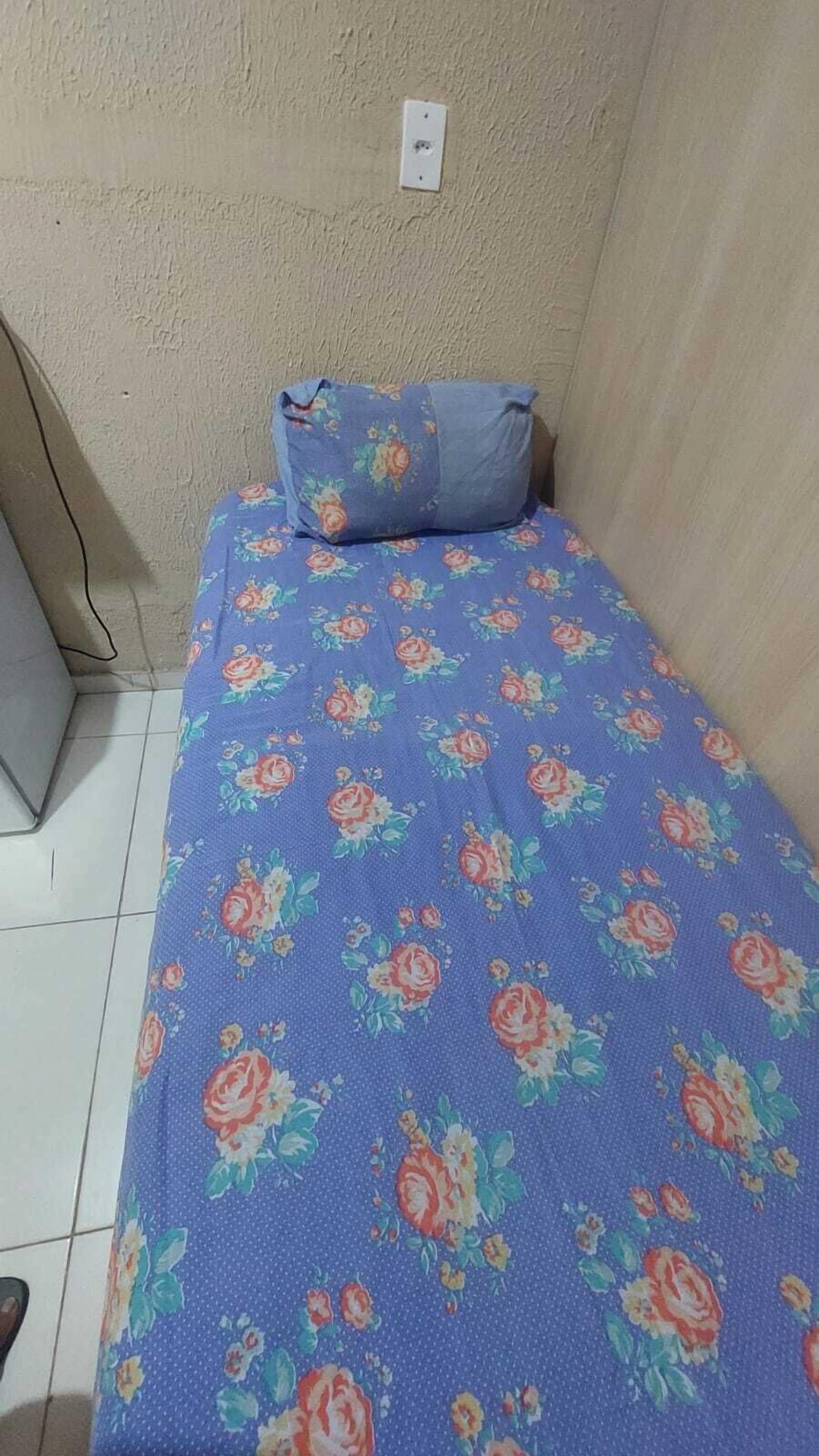 Quarto pequeno com uma cama de solteiro, coberta por um edredom estampado com flores e travesseiro combinando.