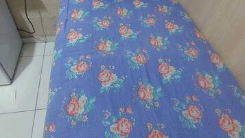 Quarto pequeno com uma cama de solteiro, coberta por um edredom estampado com flores e travesseiro combinando.
