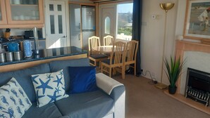 A cozy living area with a sofa, a dining table with chairs, a kitchen area with a refrigerator, and a fireplace. - Bay View - fantastic views of Whitsand Bay and the Rame Peninsula (Rame)