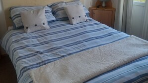 A bed with striped bedding, two pillows, a bedside table with a lamp, and a painting on the wall. - Bay View - fantastic views of Whitsand Bay and the Rame Peninsula (Rame)