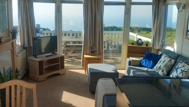 A spacious living area with a TV, seating, and large windows offering a view of the outdoors. - Bay View - fantastic views of Whitsand Bay and the Rame Peninsula (Rame)