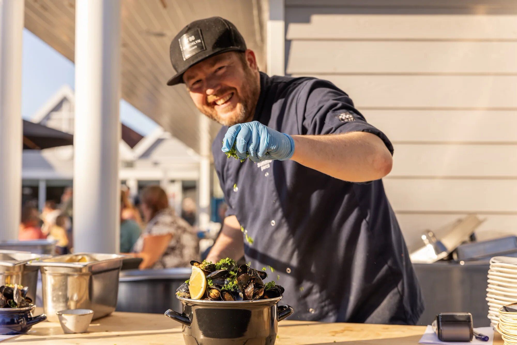 A person serving food from a pot, with a dining table and kitchen equipment in the background.