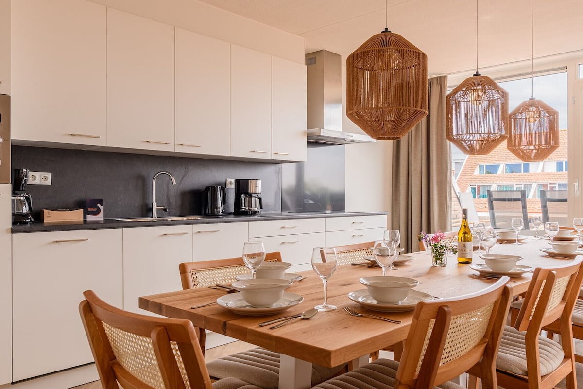 A modern kitchen with white cabinets, a black countertop, and a dining area with a wooden table and chairs.