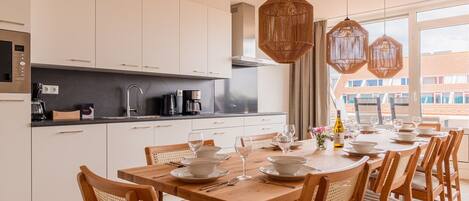 A modern kitchen with white cabinets, a black countertop, and a dining area with a wooden table and chairs.