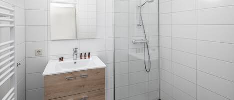 A modern bathroom with a white sink, wooden cabinet, and a glass shower enclosure.