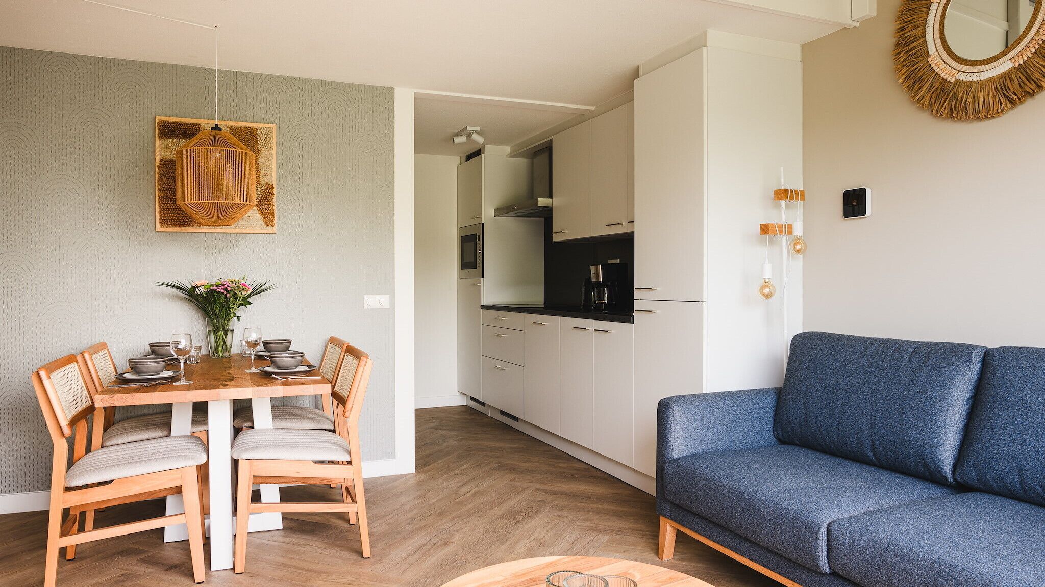 A modern kitchen with white cabinets, a dining area with a wooden table and chairs, and a blue sofa.