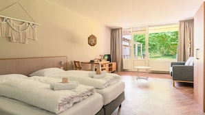 Habitación de hotel con dos camas, un escritorio, una silla y vistas a zonas verdes por la ventana.