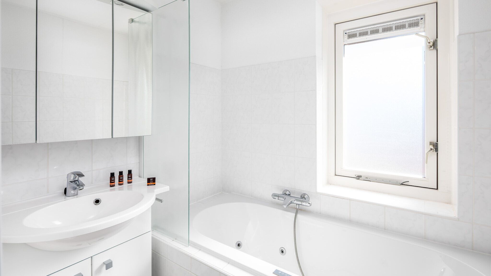 A modern bathroom with a white sink, mirror, and bathtub.