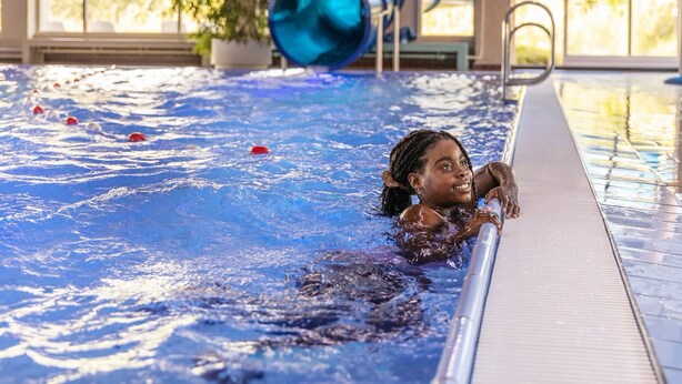Una piscina con una persona nadando, un objeto cilíndrico azul y una planta al fondo.