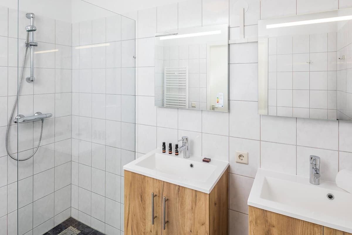 A modern bathroom with a shower, two sinks, and wooden cabinets.