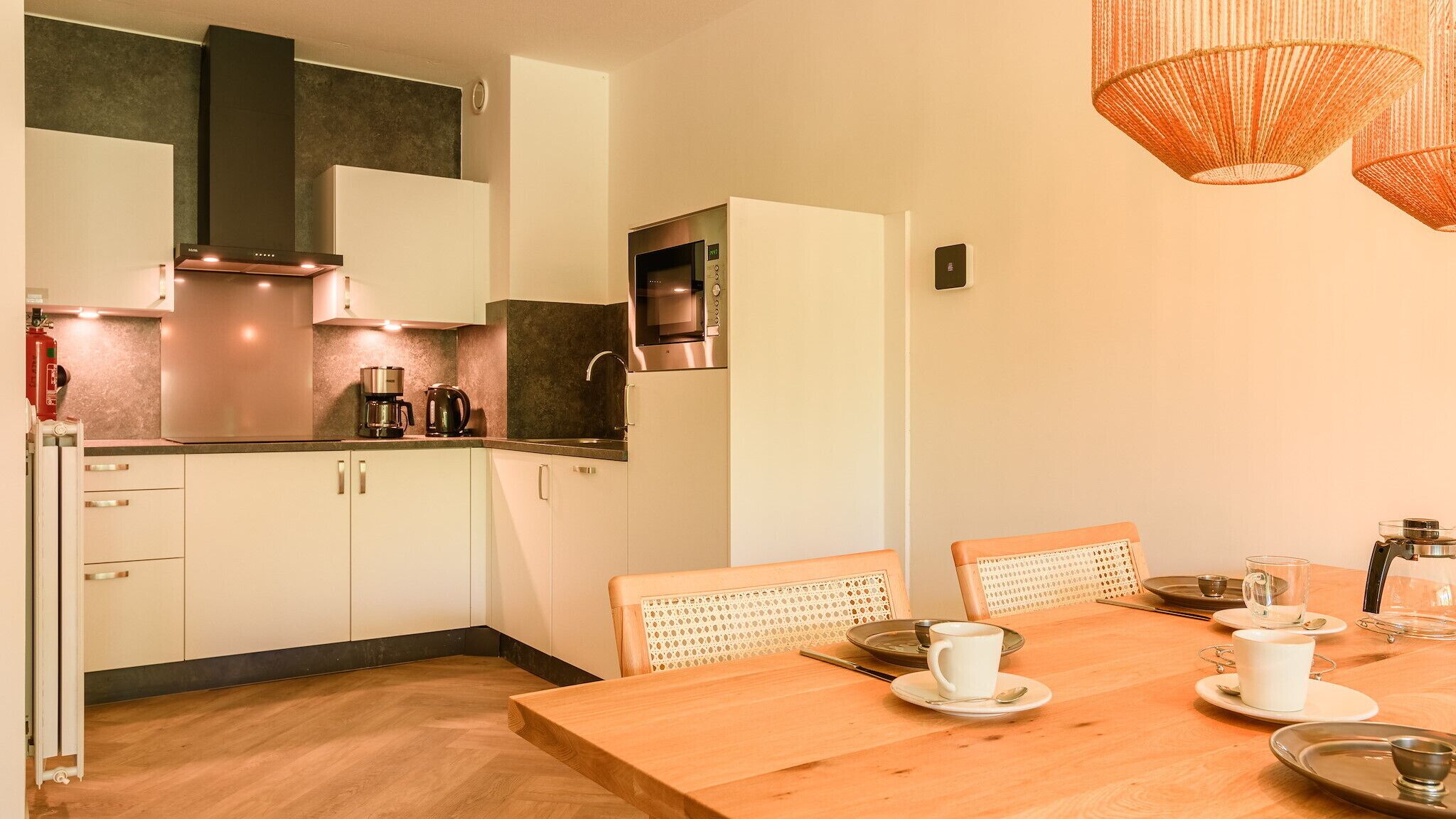 A modern kitchen with white cabinets, stainless steel appliances, and a wooden dining table set for two.
