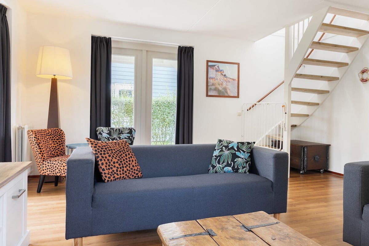 A living room with a sofa, two armchairs, a wooden coffee table, a lamp, and a staircase leading to an upper level.