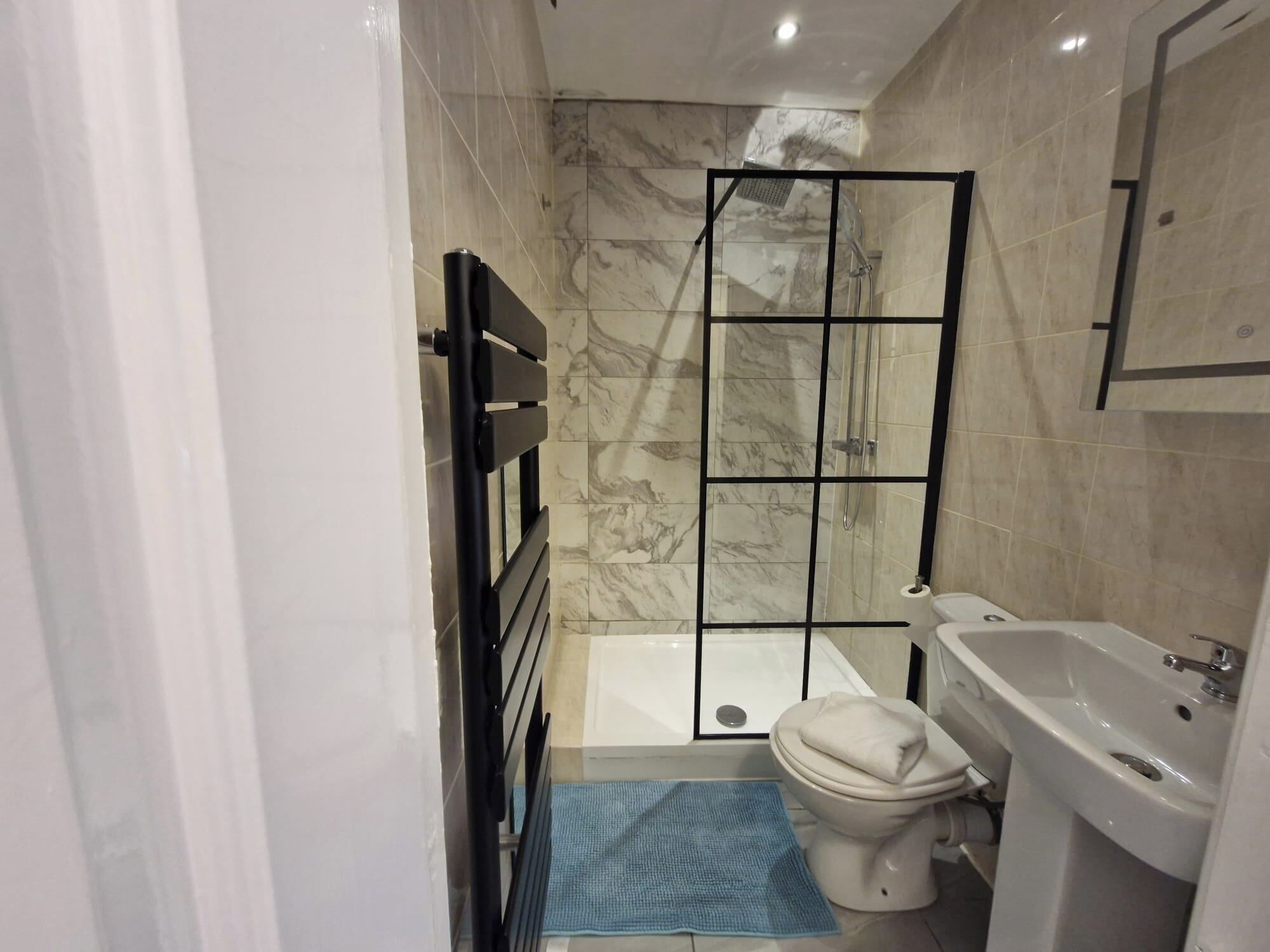 A bathroom with a shower enclosure, toilet, sink, and a blue mat on the floor.