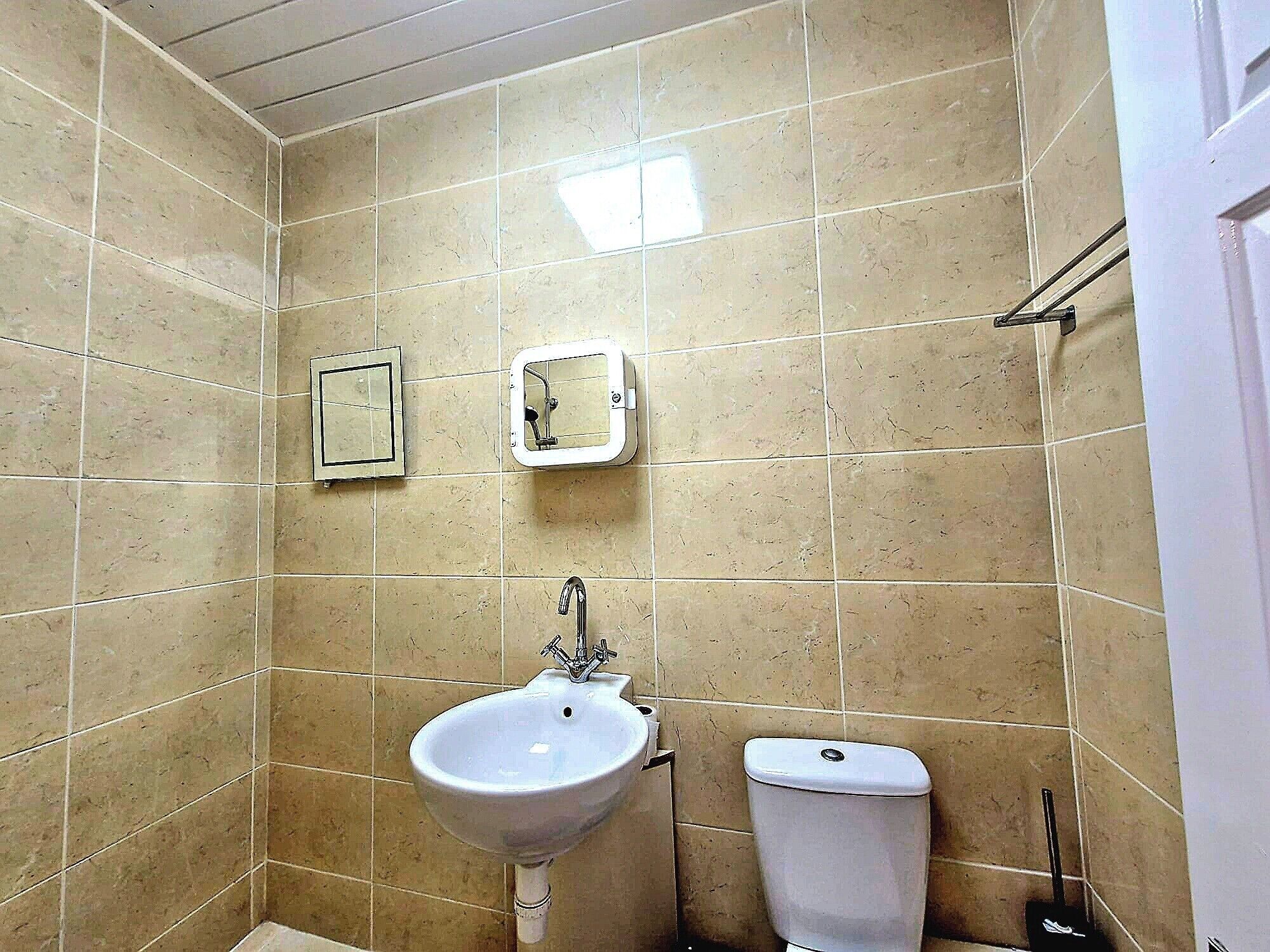A bathroom with beige tiled walls, a white sink, and a toilet.