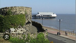 A stone wall with greenery, a waterfront promenade, and a pier with a building. - Seaside Bliss Apartment for Style and Comfort (Cleethorpes)
