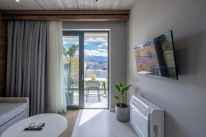 Una sala de estar moderna con sofá, mesa de centro, televisor montado en la pared y puerta corrediza de vidrio que da a un balcón con vistas a edificios y montañas.