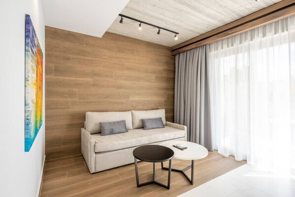 Una sala de estar moderna con un sofá color beige, una mesa redonda de centro y un ventanal con cortinas traslúcidas.