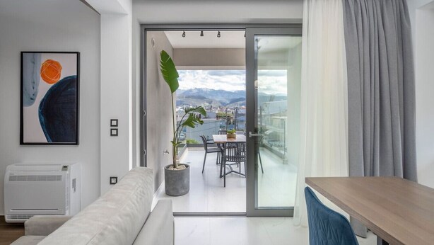 A modern living room with a sofa, a dining table, and a balcony with a view of the mountains.