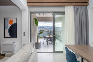 A modern living room with a sofa, a dining table, and a balcony with a view of the mountains. - Disegno Suite 2 | Jacuzzi | Chania City Center (Chania)