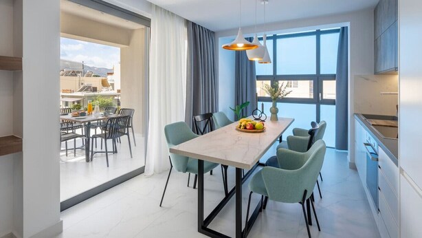 A modern dining area with a marble table, six chairs, and a fruit bowl.