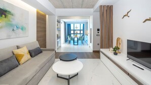 A modern living room with a sofa, coffee table, TV, and artwork.