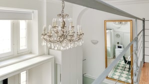 Een trap met een kroonluchter, een spiegel en uitzicht op een kamer met een geruit vloerkleed.