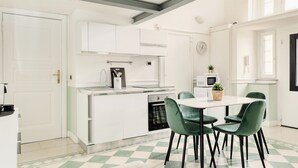 Een moderne keuken met witte kasten, een eettafel met groene stoelen en een geruit vloertje.