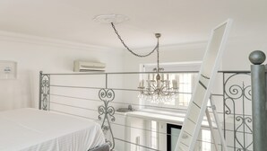 Een slaapkamer met een bed, een kroonluchter, een ladder en een raam met gordijnen.