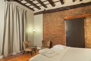 A room with a bed, two chairs, a curtain, a floor lamp, and a brick wall.