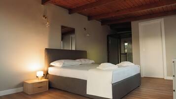 A bedroom with a wooden ceiling, a bed with white bedding, a nightstand with a lamp, and a door to another room.