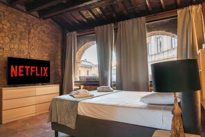 A hotel room with a bed, a television displaying 'NETFLIX', a window with curtains, and a lamp. - CB Rooms Campo Dei Fiori (Rome)