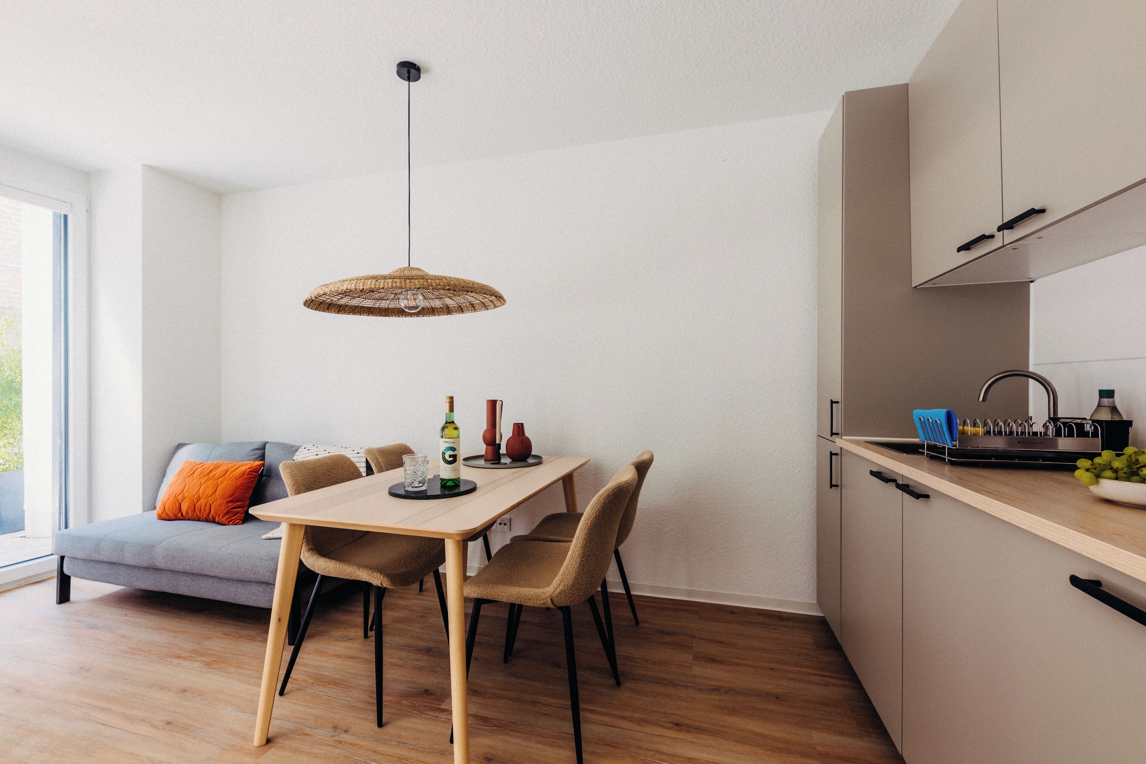 A modern kitchen with a dining area, wooden flooring, and a large window.