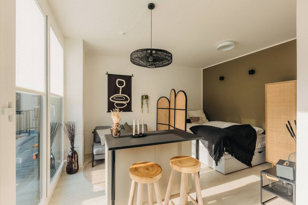 Una stanza moderna e luminosa, con un'ampia finestra, un'area pranzo con sgabelli, un letto e un piccolo tavolo con candele.