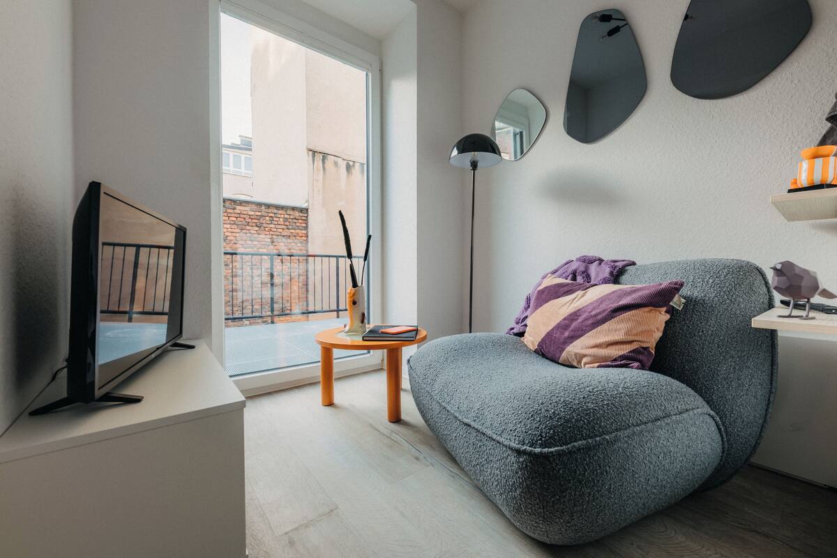 Un soggiorno moderno con un divano grigio, una TV a schermo piatto, un piccolo tavolino in legno e una lampada da terra.