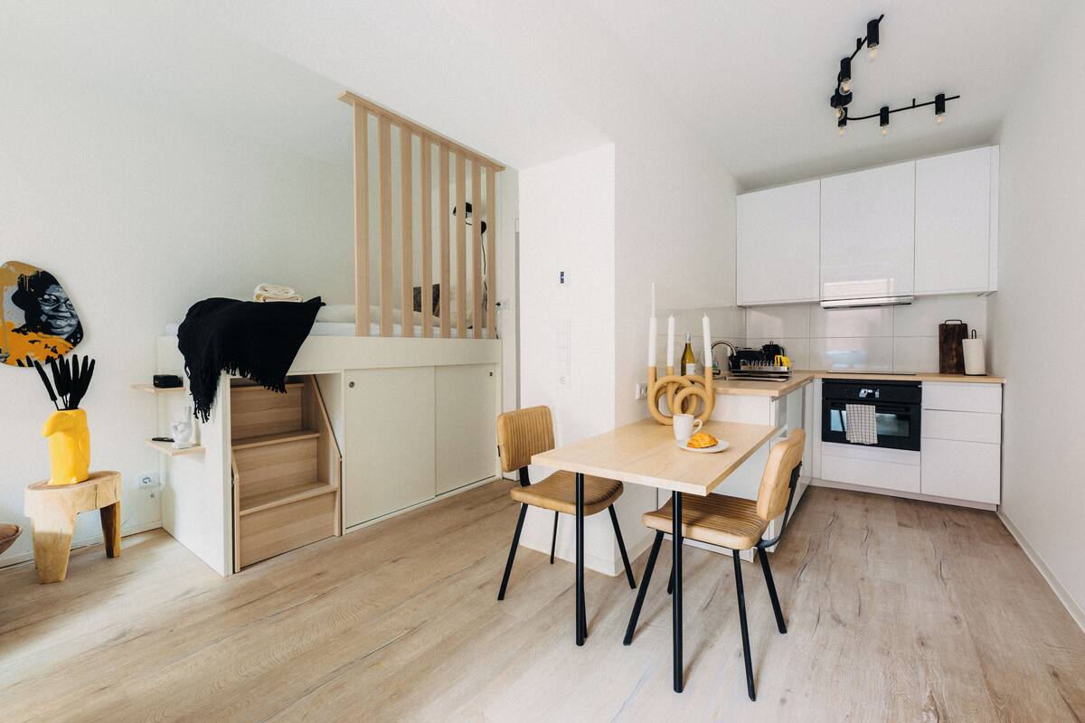 Una cucina moderna con mobili bianchi, un tavolo da pranzo in legno e una scala che conduce a una mansarda.