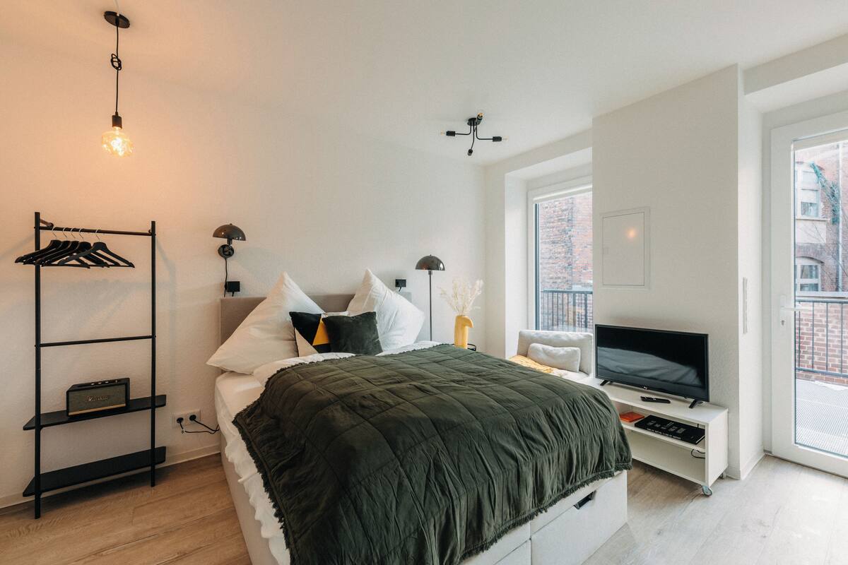 Una camera da letto moderna con un letto, una TV, uno scaffale con vestiti e una finestra.