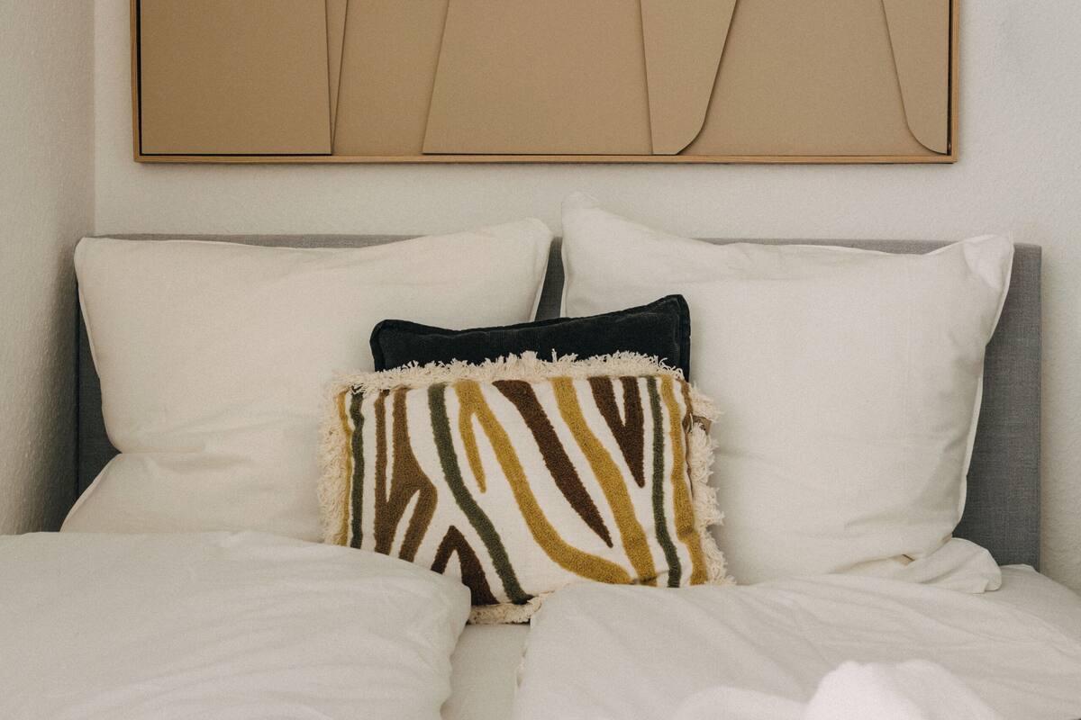 Un letto rifatto con lenzuola bianche e nere, un cuscino a motivi zebrati e un asciugamano bianco piegato su una coperta blu scuro.