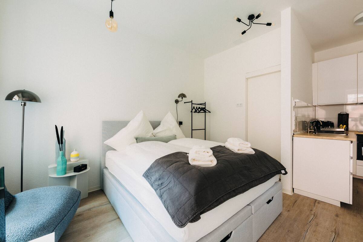 Una camera da letto moderna con un letto, un comodino, una lampada e un angolo cottura.