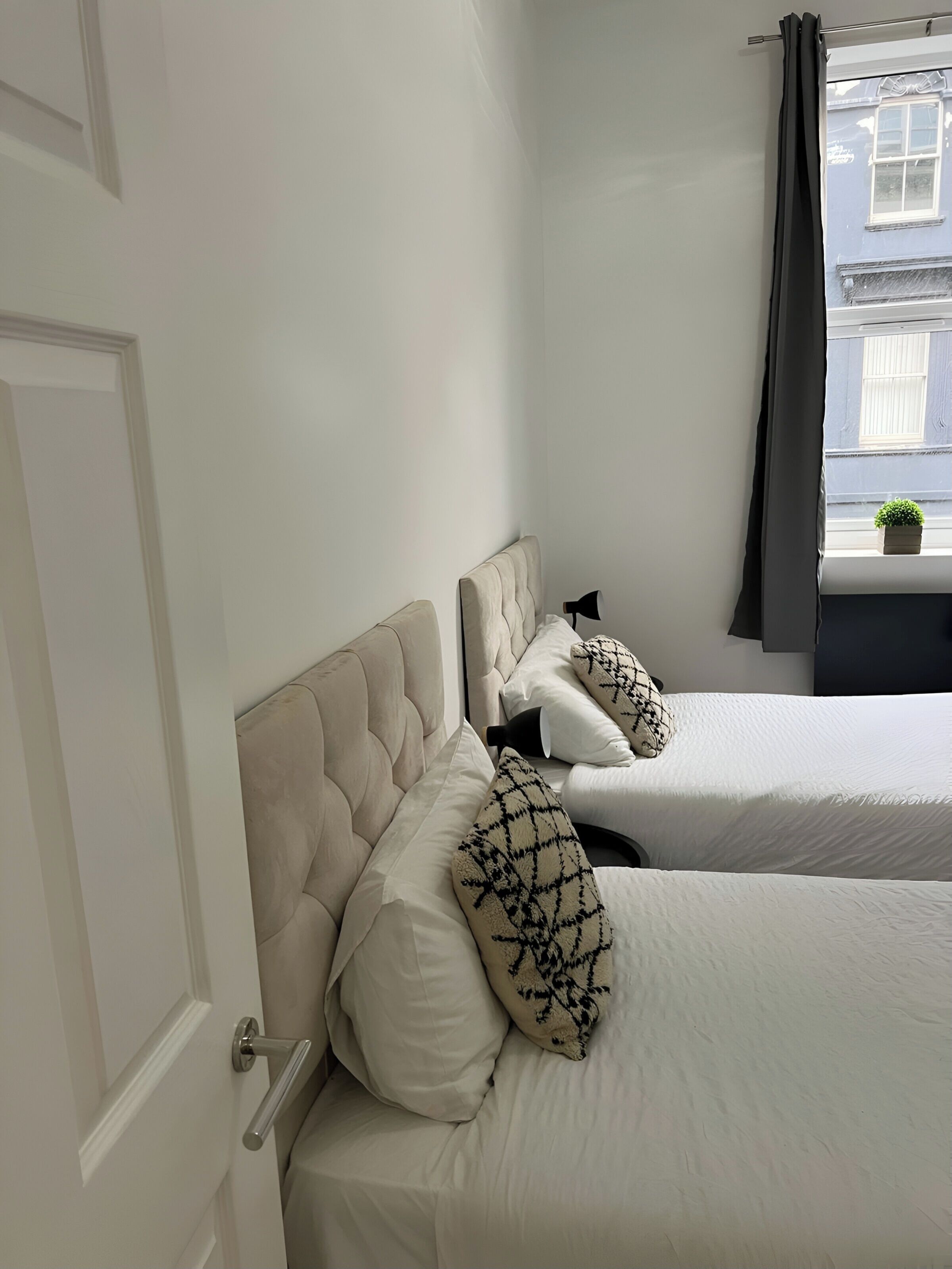 Een hotelkamer met twee bedden, elk met een gestoffeerd hoofdeinde en gestreepte kussens.