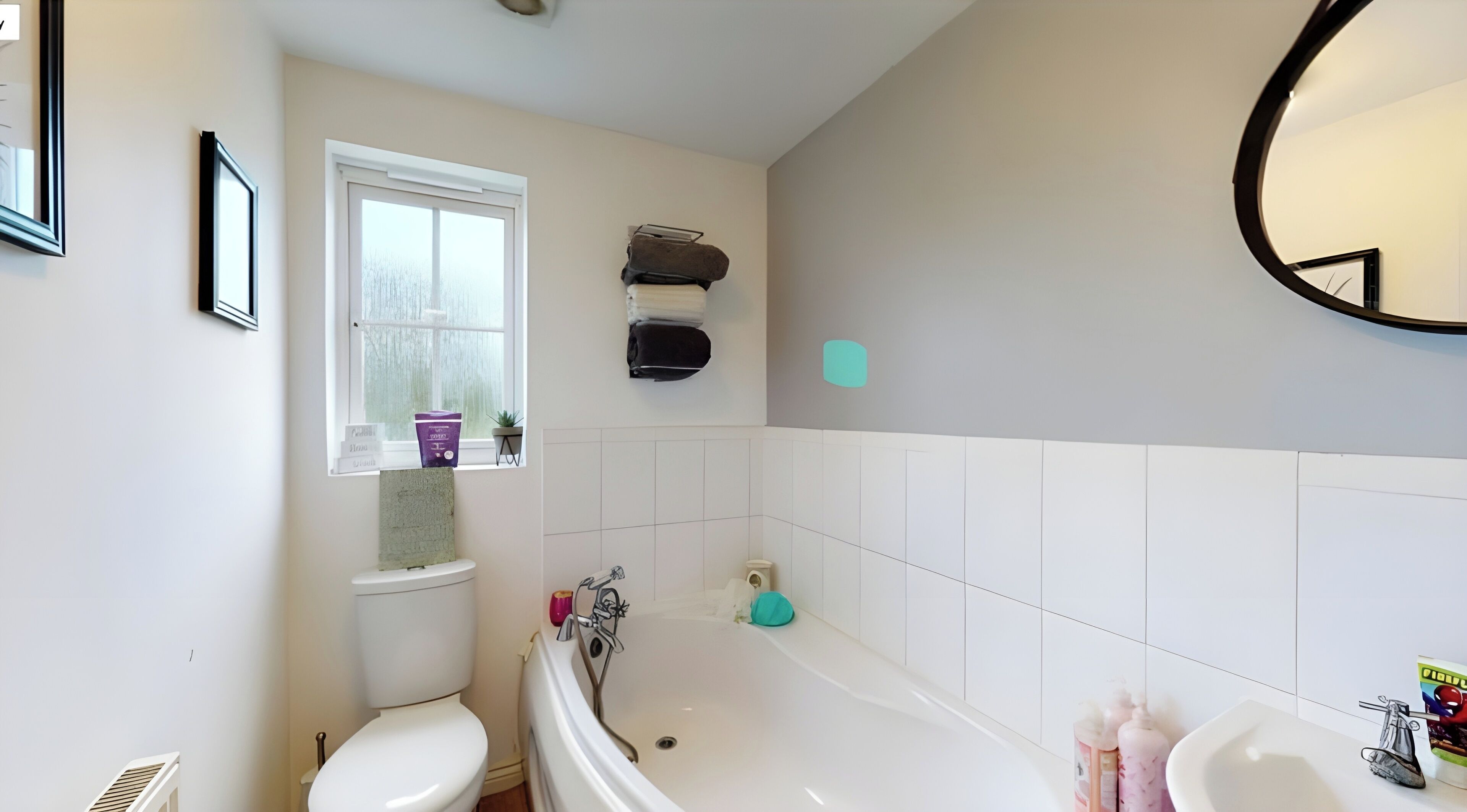 A bathroom with a toilet, sink, and bathtub. There is a window with a view of trees, a towel rack, and a potted plant.