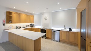 A modern kitchen with wooden cabinets, a central island, built-in oven, dishwasher, and stainless steel appliances. - Heathercroft Apartment-Modern Comfort in Fort William. (Fort William)